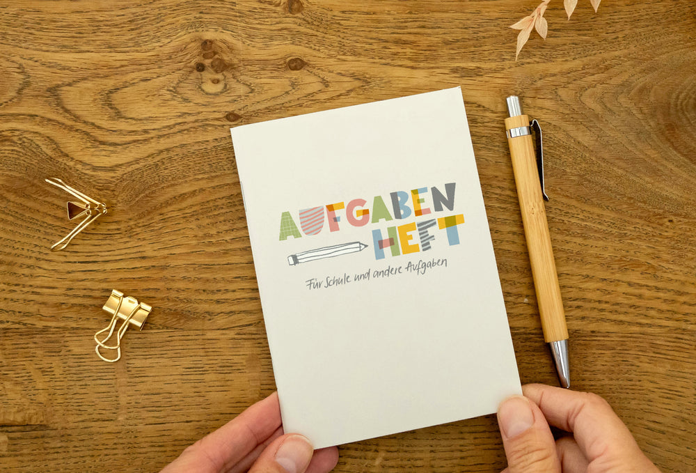 Hausaufgabenheft A6 liegt auf Holztisch neben Stift und goldenen Büroklammern