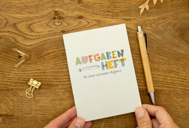 Hausaufgabenheft A6 liegt auf Holztisch neben Stift und goldenen Büroklammern