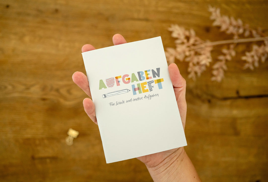 Hand hält das kleine Hausaufgabenheft A6 „Aufgabenheft – Für Schule und andere Aufgaben“