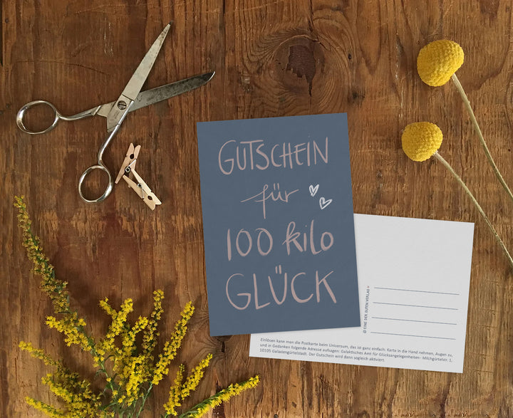 Gutschein für 100 Kilo Glück Glückwunschkarte als kleine Aufmerksamkeit im Alltag, dekorativ auf einem Tisch platziert